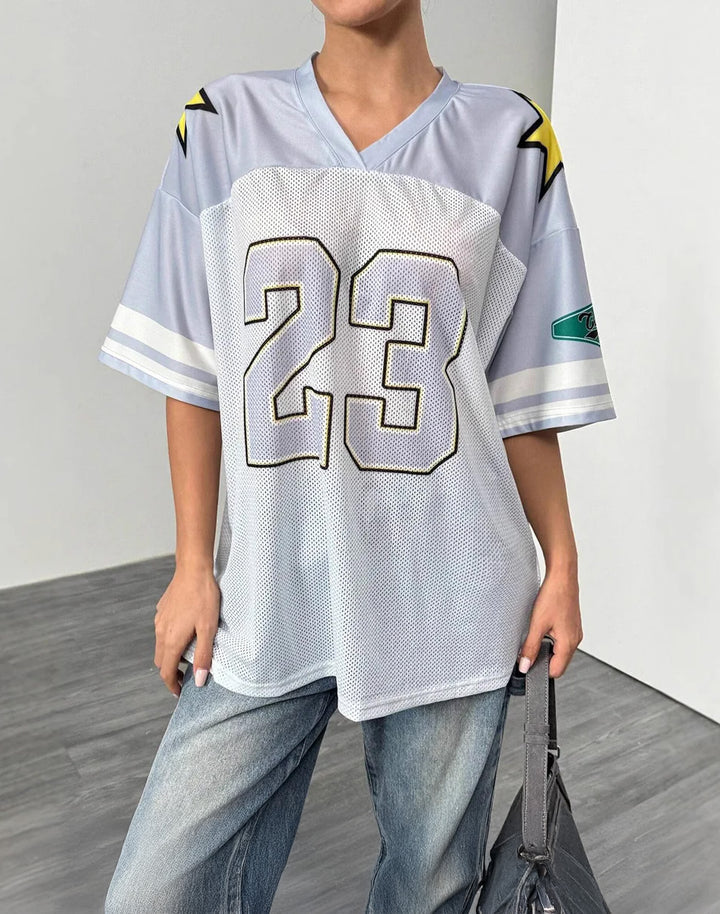 Light grey and white Y2K oversized jersey with a bold '23' print and sporty star accents. Breathable mesh fabric, styled casually with denim for a relaxed streetwear aesthetic.