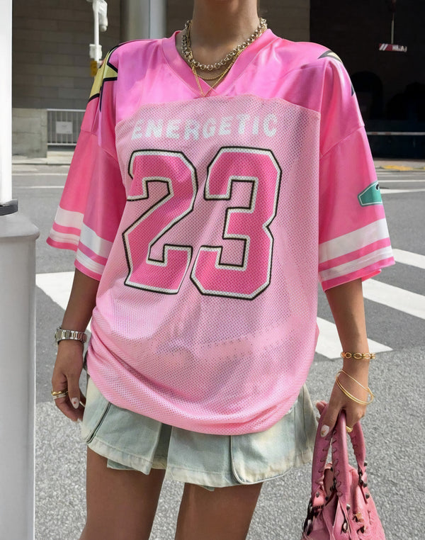 Pink varsity-style Y2K jersey with bold '23 Energetic' print, styled with a pleated denim skirt for a cute and sporty streetwear outfit. Breathable and lightweight