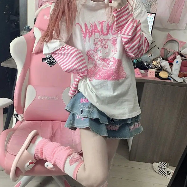 Girl wearing an oversized Hello Kitty Harajuku Punk Layered T-Shirt with pink and white striped long sleeves, paired with a denim skirt adorned with Hello Kitty graphics, in a kawaii-themed room.