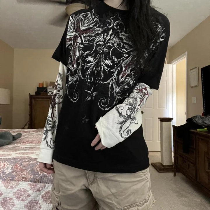 Gothic t-shirt with layered-look white long sleeves, featuring intricate cross and wing designs, styled casually by a model wearing cargo shorts.