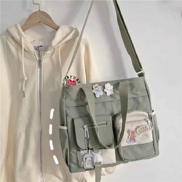 Green Kawaii Multi-Pocket Nylon Shoulder Bag hanging on a hook, featuring multiple front pockets with cute accessories, perfect for casual and kawaii fashion.