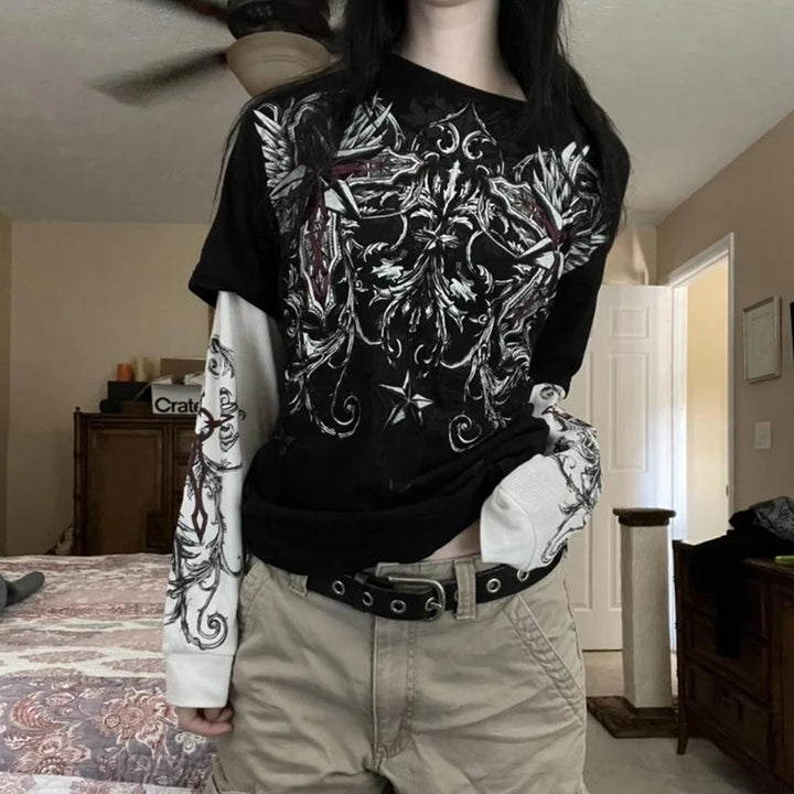 E-girl wearing a black gothic long sleeve t-shirt with layered sleeves, bold cross and wing designs, paired with cargo shorts in an alternative fashion style.