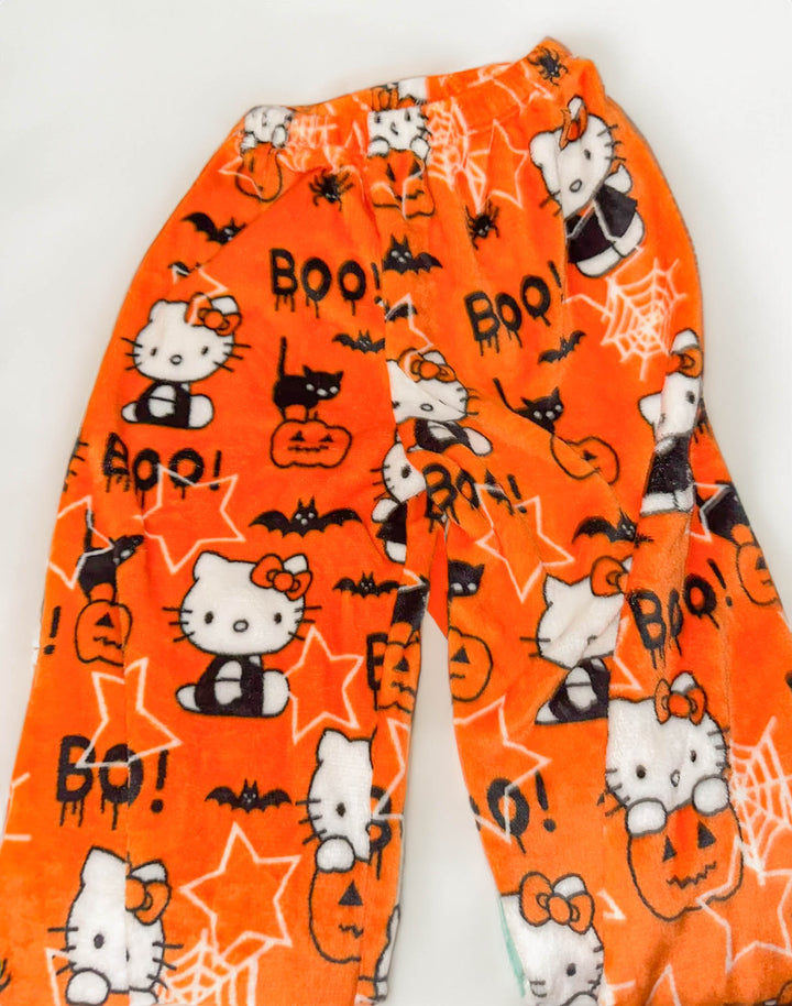 Close-up of Hello Kitty Halloween pajama pants with cute vampire Hello Kitty print, black cats, pumpkins, and bats on a bright orange plush fabric.